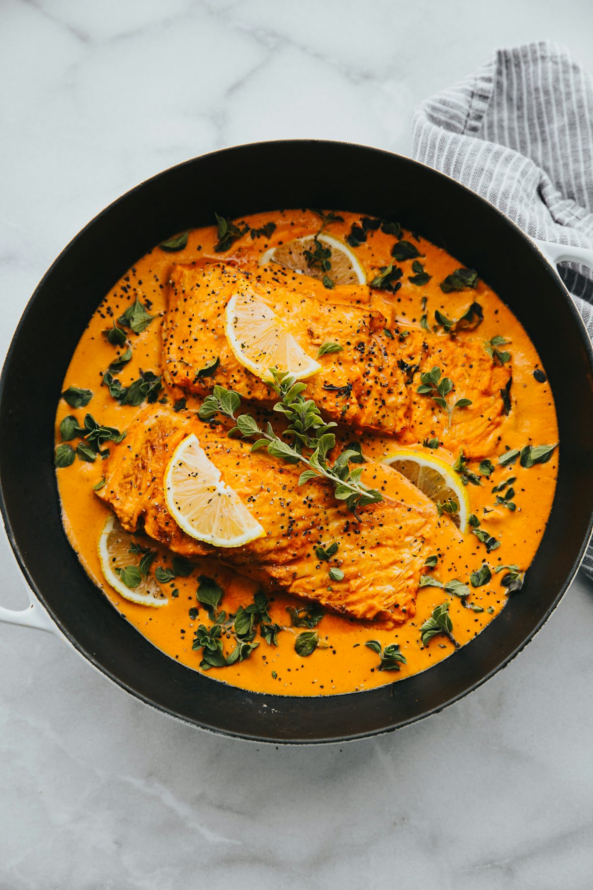 Filets de poisson nappés d’une sauce safranée, citron et herbes, dans une poêle noire